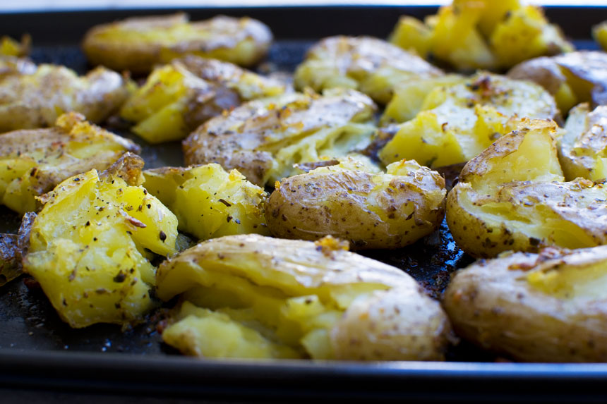 A closeup of Greek style crispy smashed potatoes on a baking tray