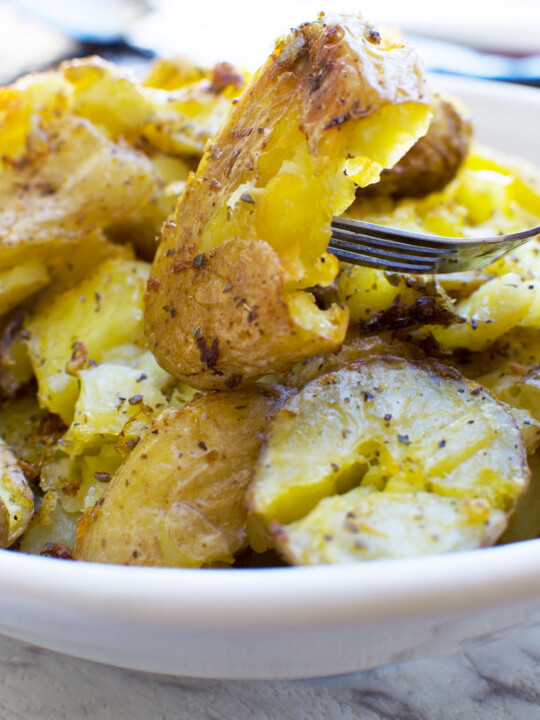 A close up of a Greek style crispy smashed potato on a fork over a whole bowl of them
