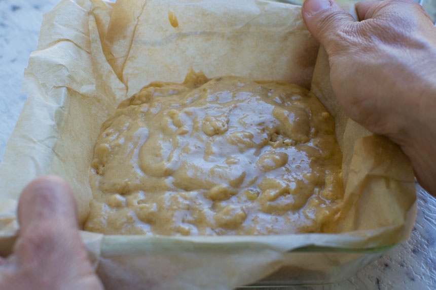 Someone holding a raw mini banana bread in a loaf pan 