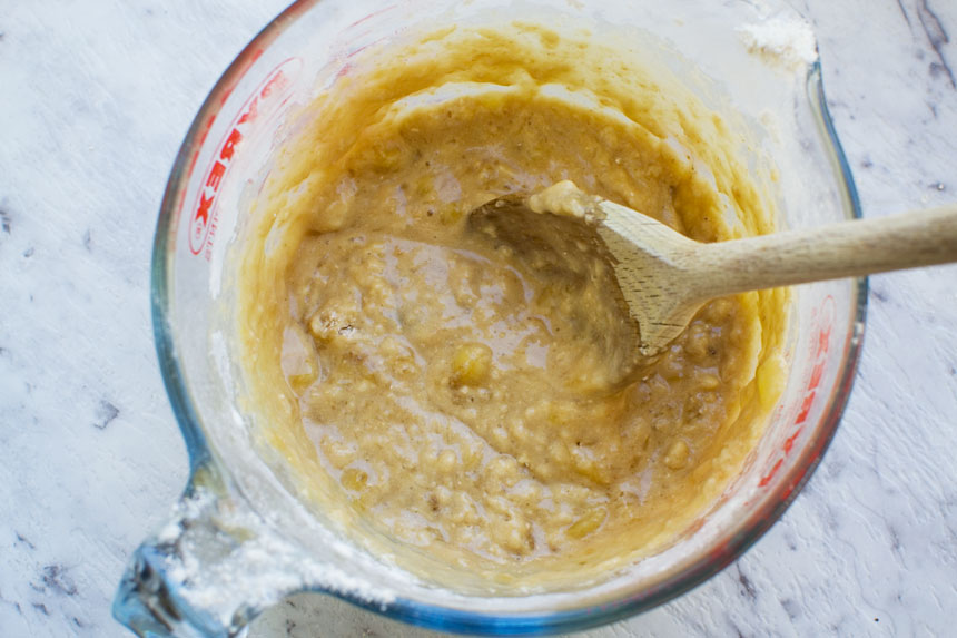 Batter for Quick and easy mini banana bread in a Pyrex jug from above with a wooden spoon