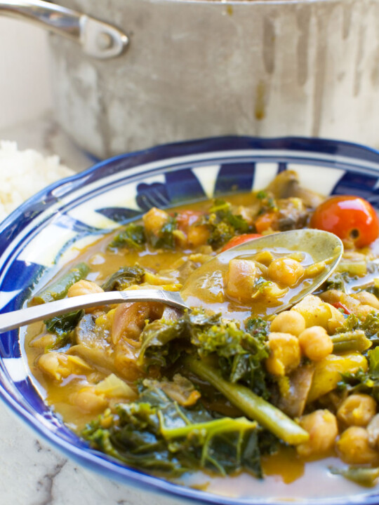 A bowl of 20-minute coconut chickpea curry with a spoon in it and rice in the background