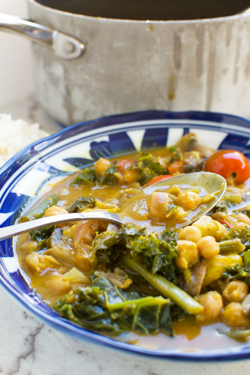 A bowl of 20-minute coconut chickpea curry with a spoon in it and rice in the background