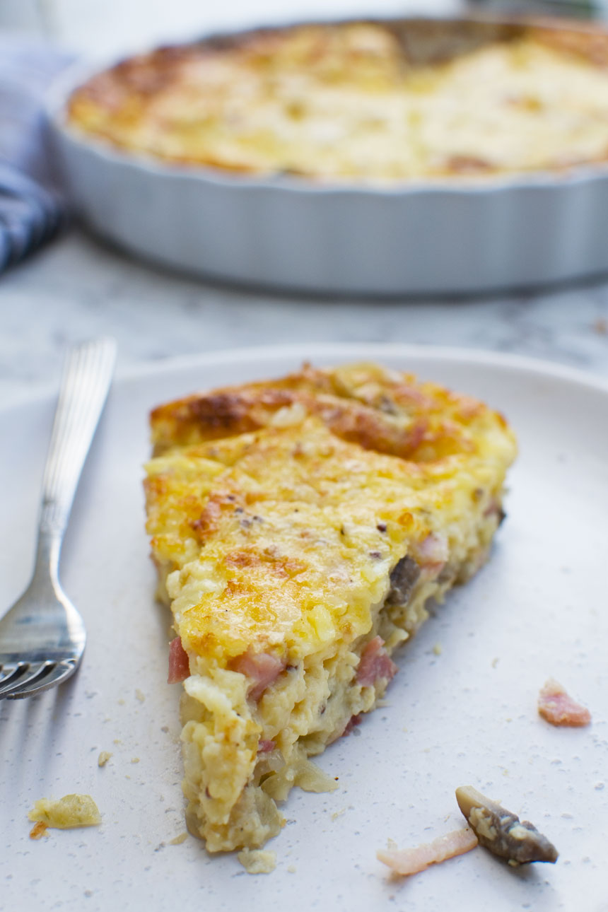 A close up of a slice of quiche on a white plate with a fork