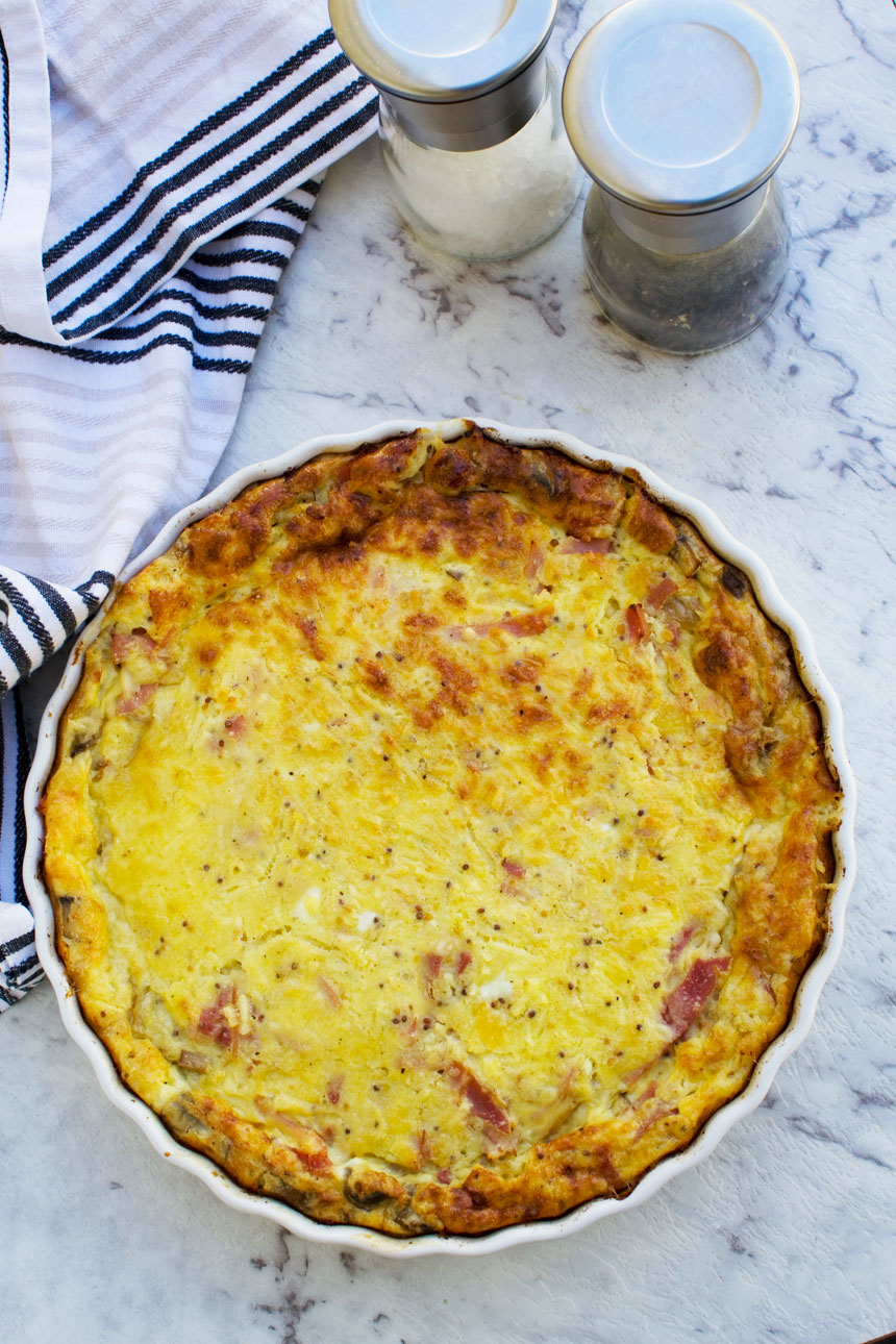 A whole crustless quiche from above on a white background with a blue tea towel in the background