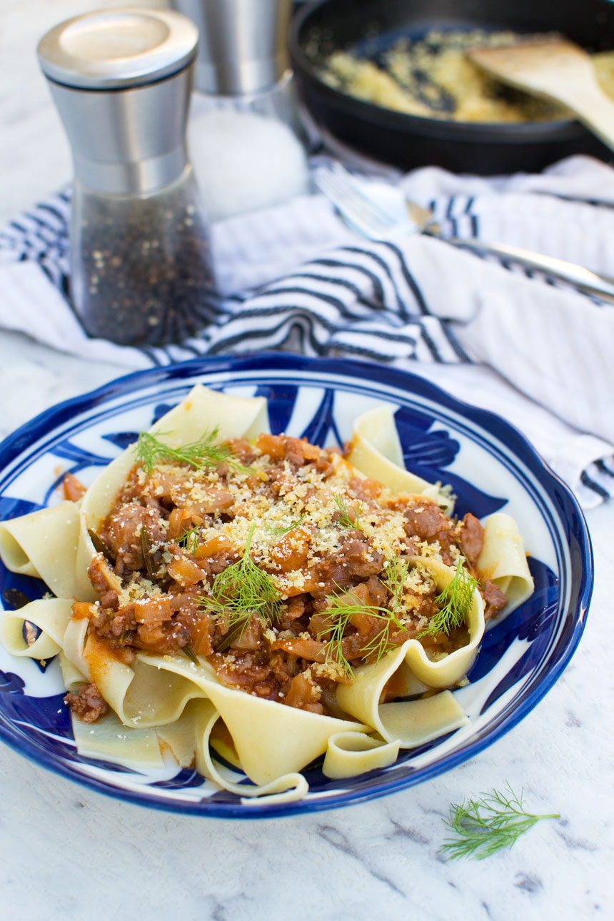 A plate of 6-ingredient sausage fennel bolognese on a blue plate with a blue striped tea towel in the background