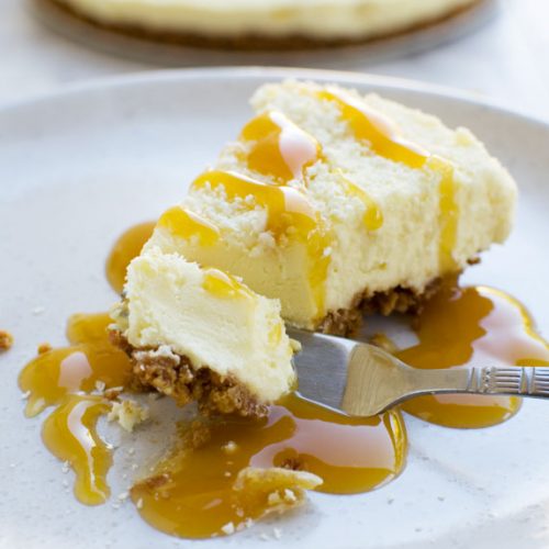 A piece of ginger and white chocolate cheesecake on a white plate being eaten with a fork