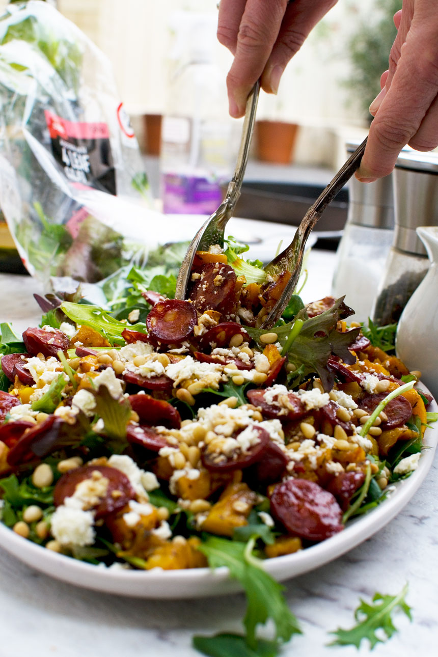 A person serving an Amazing Roast Pumpkin, Chorizo And Feta Salad with salad servers