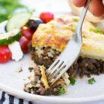 Someone eating a piece of easy moussaka with a fork - there's some Greek salad in the background