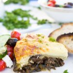 A piece of easy moussaka on a white plate with bread and Greek salad