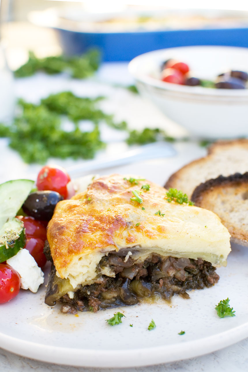 A piece of easy moussaka on a white plate with bread and Greek salad 