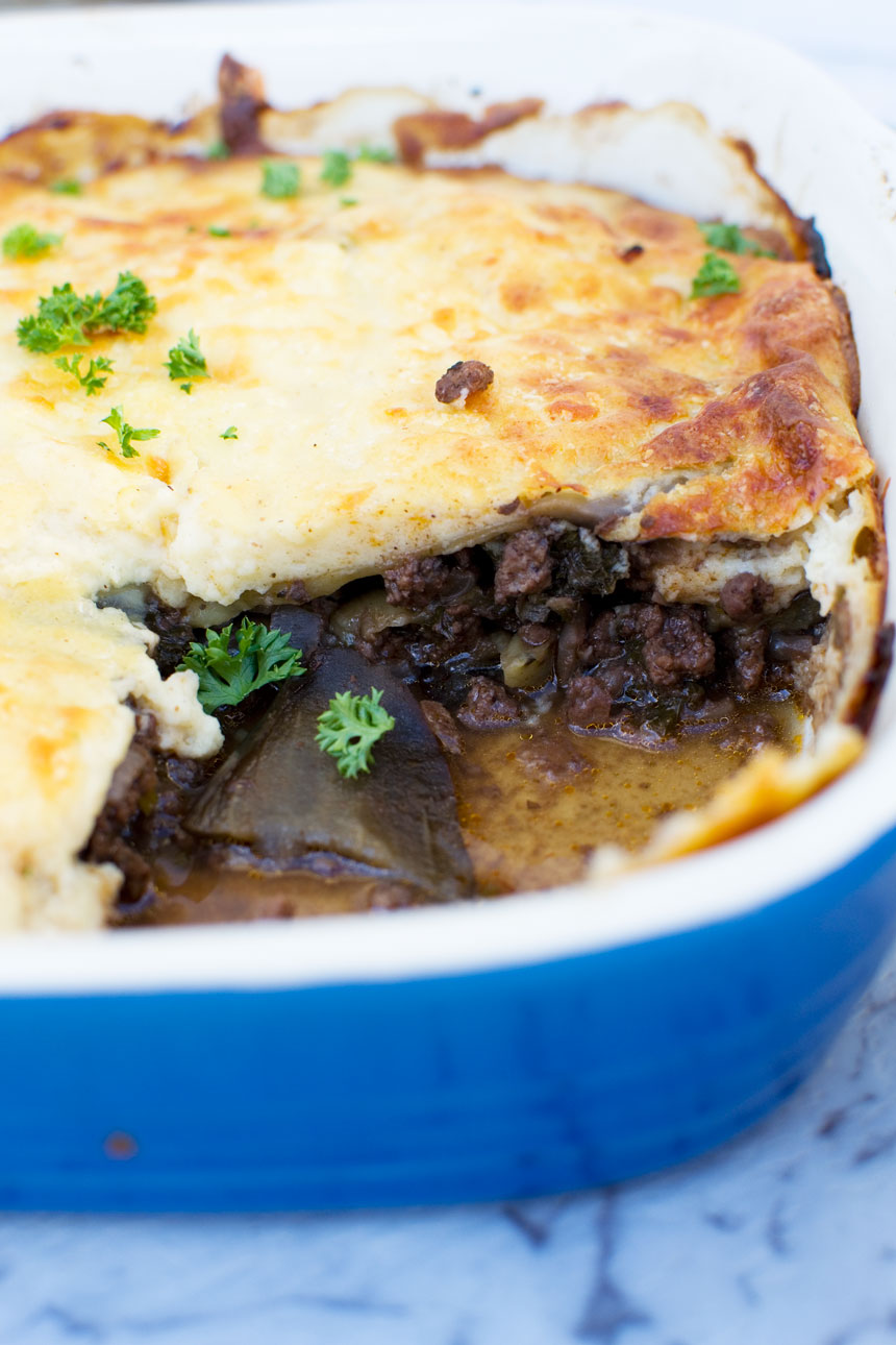 A close up of a blue baking dish of Greek moussaka with a piece cut out of it