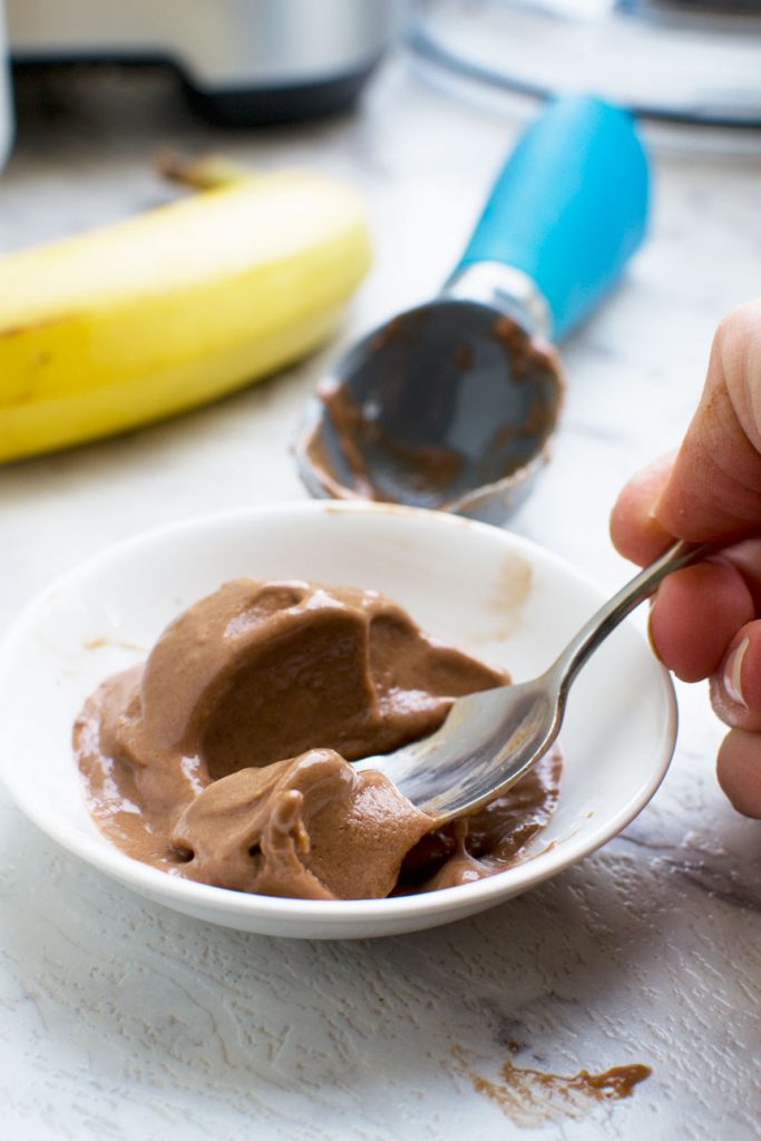 Somone eating 5-minute chocolate banana ice cream with a spoon - there\'s an ice cream scoop and a banana in the background