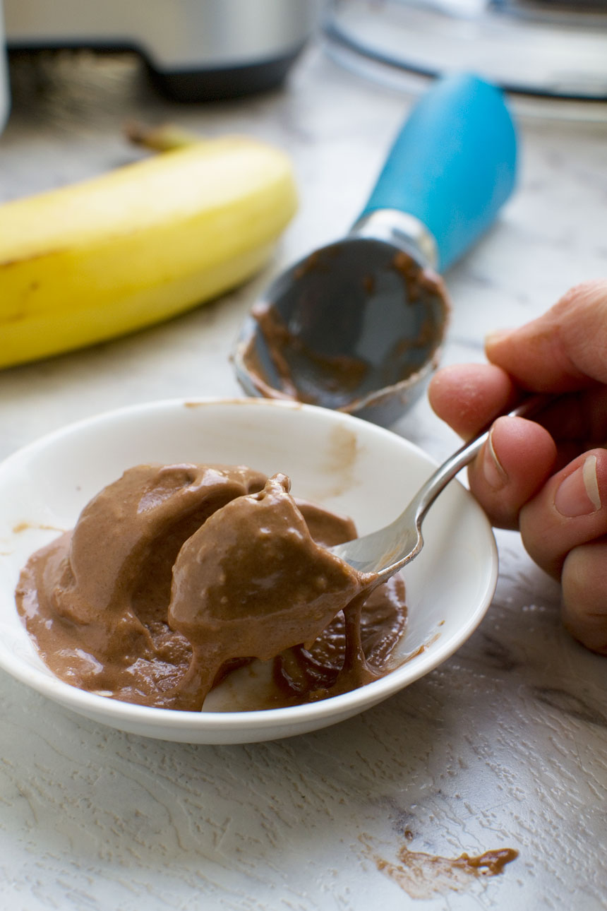 Close up of someone eating 5-minute chocolate banana ice cream with a spoon with a banana and ice cream scoop in the background