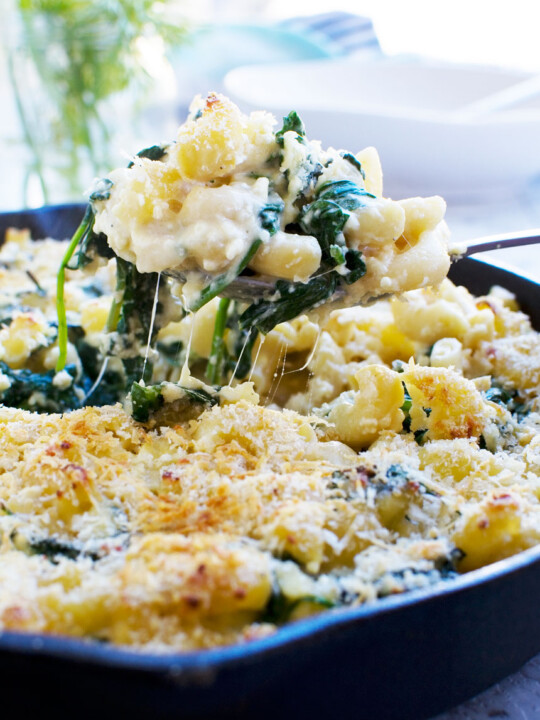 Someone serving a big spoon of Greek mac and cheese bake out of a black cast iron pan