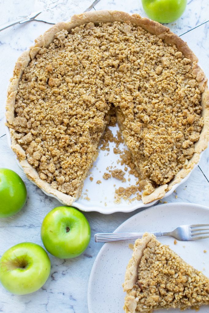 A whole apple crumble pie (Dutch apple pie) with a piece cut out of it from above with green apples next to it