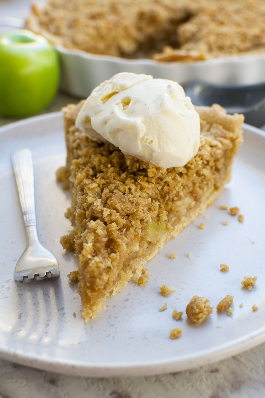 A close up of a piece of apple crumble pie on a white plate with a fork