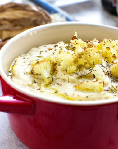 A small red cast iron pot of cauliflower and potato mashed potatoes garnished with roasted cauliflower