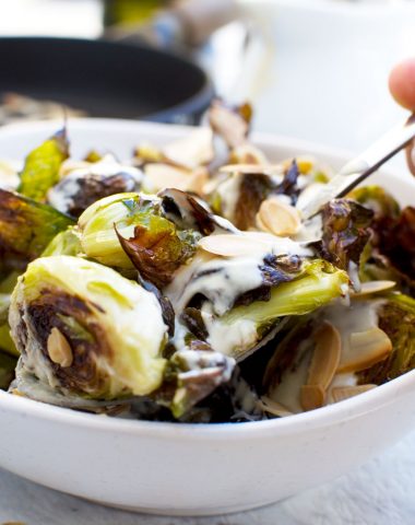 Someone serving themselves from a dish of crispy brussels sprouts with tahini sauce and almonds