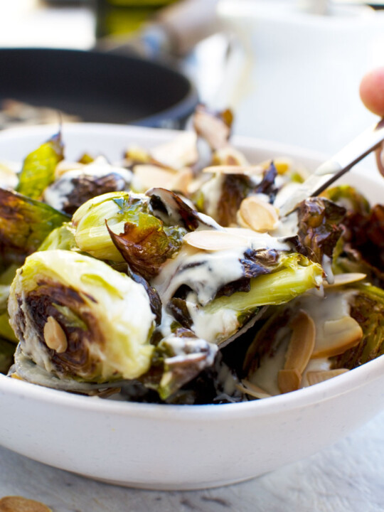 Someone serving themselves from a dish of crispy brussels sprouts with tahini sauce and almonds