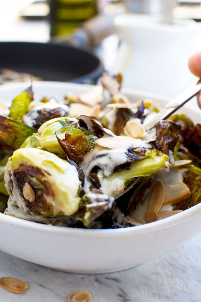 Someone serving themselves from a dish of crispy brussels sprouts with tahini sauce and almonds
