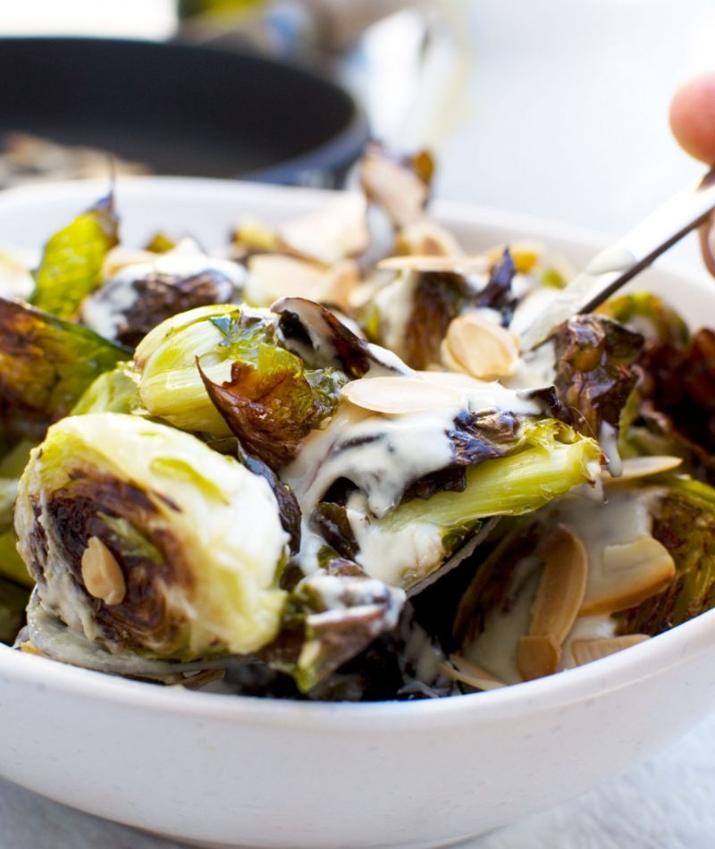 Someone serving themselves from a dish of crispy brussels sprouts with tahini sauce and almonds