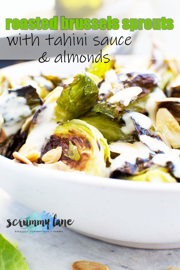 A close up of a white bowl of roasted brussels sprouts with tahini sauce and almonds for Pinterest