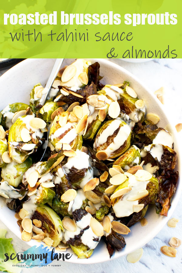 An overhead of a white bowl of roasted brussels sprouts with tahini sauce and almonds