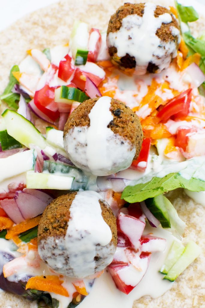 A close up of the inside of a falafel wrap drizzled with tahini dressing