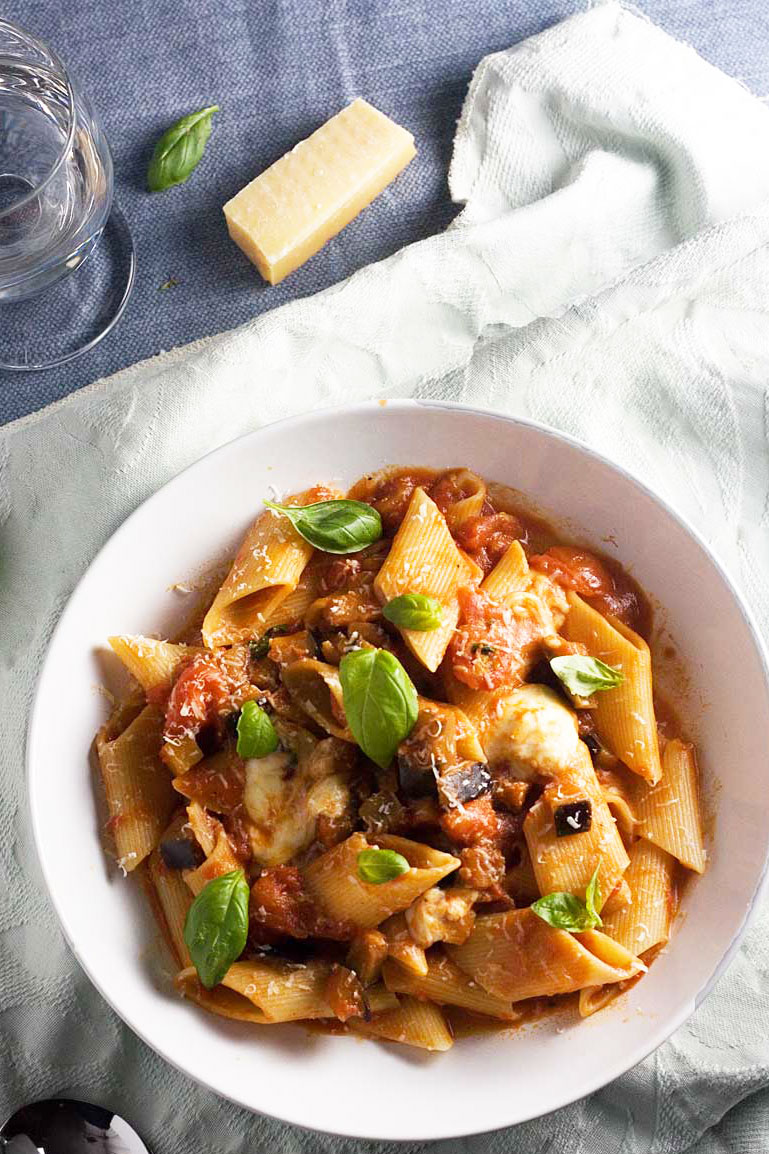 A bowl of pasta alla norma or tomato and eggplant pasta from above on a light green cloth