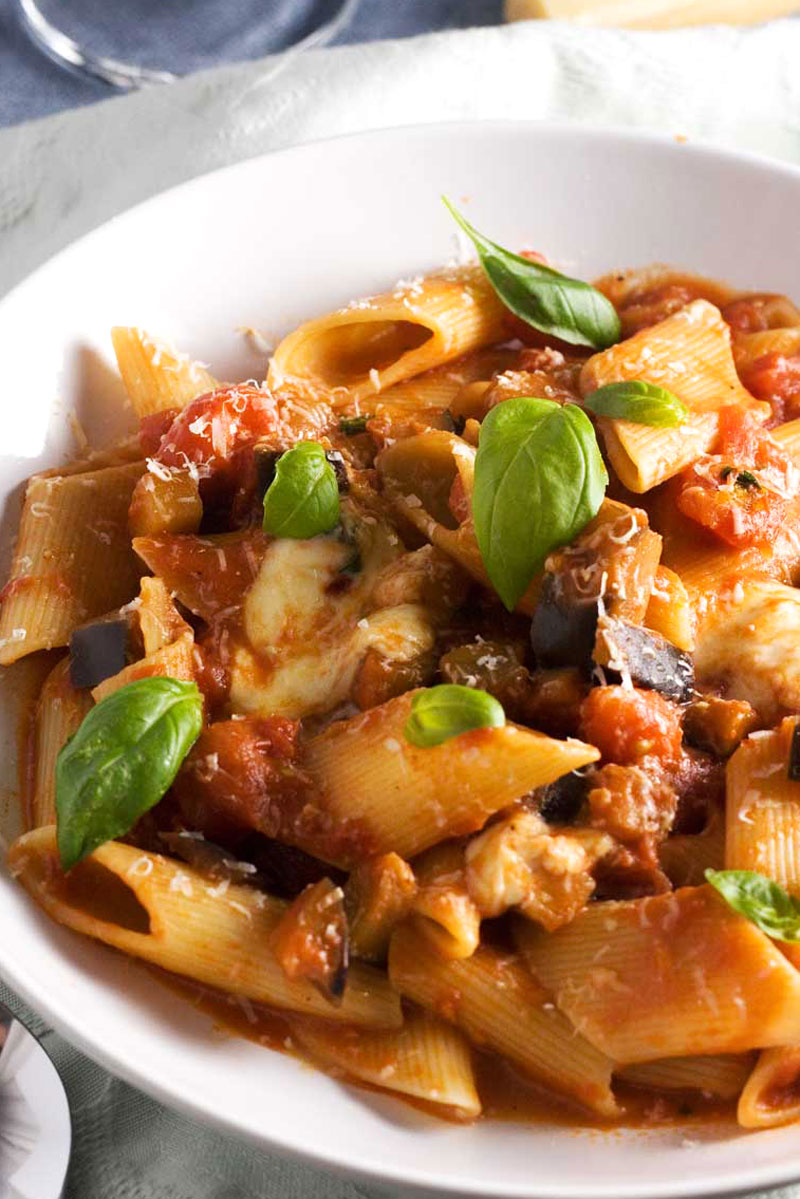 A close up of a white bowl of Pasta alla Norma garnished with basil