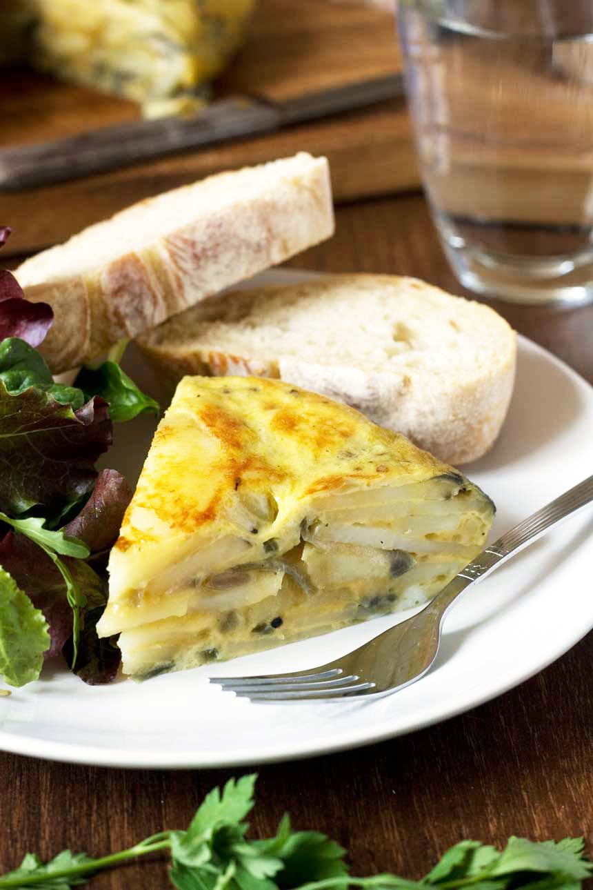 A slice of Spanish omelette on a white plate with green salad