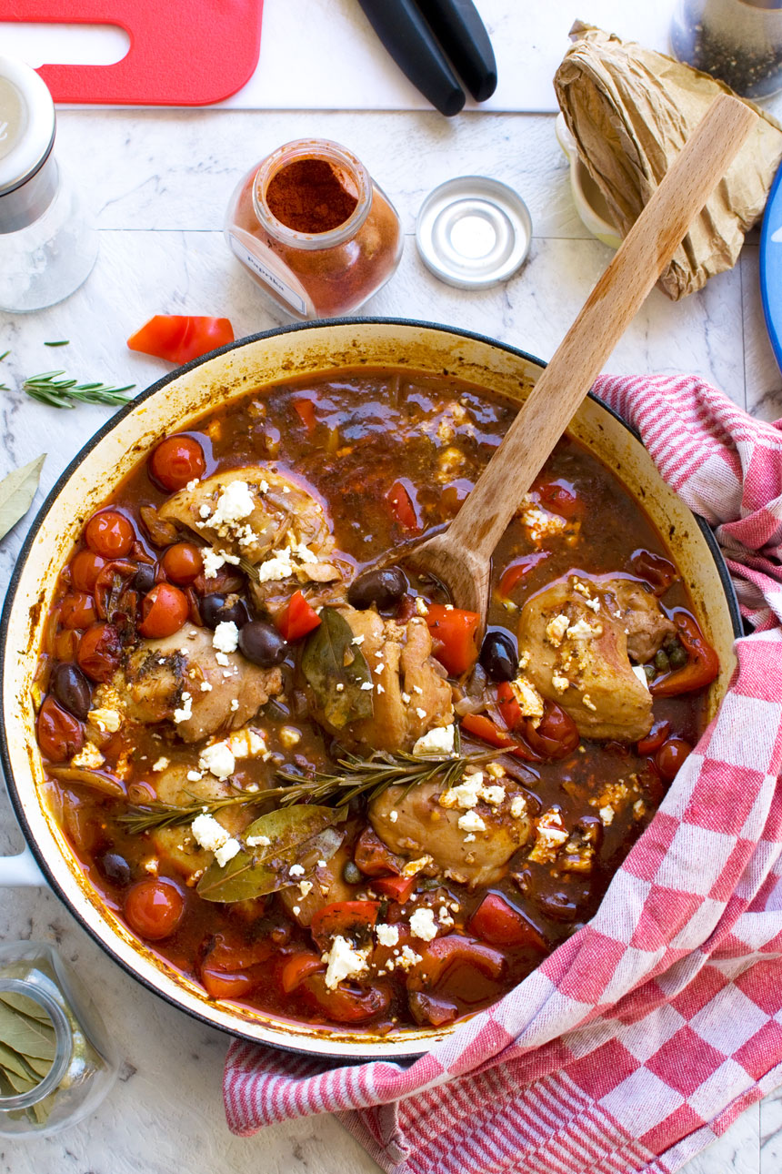 A Mediterranean stove top chicken casserole in a cast iron pan with ingredients surrounding it