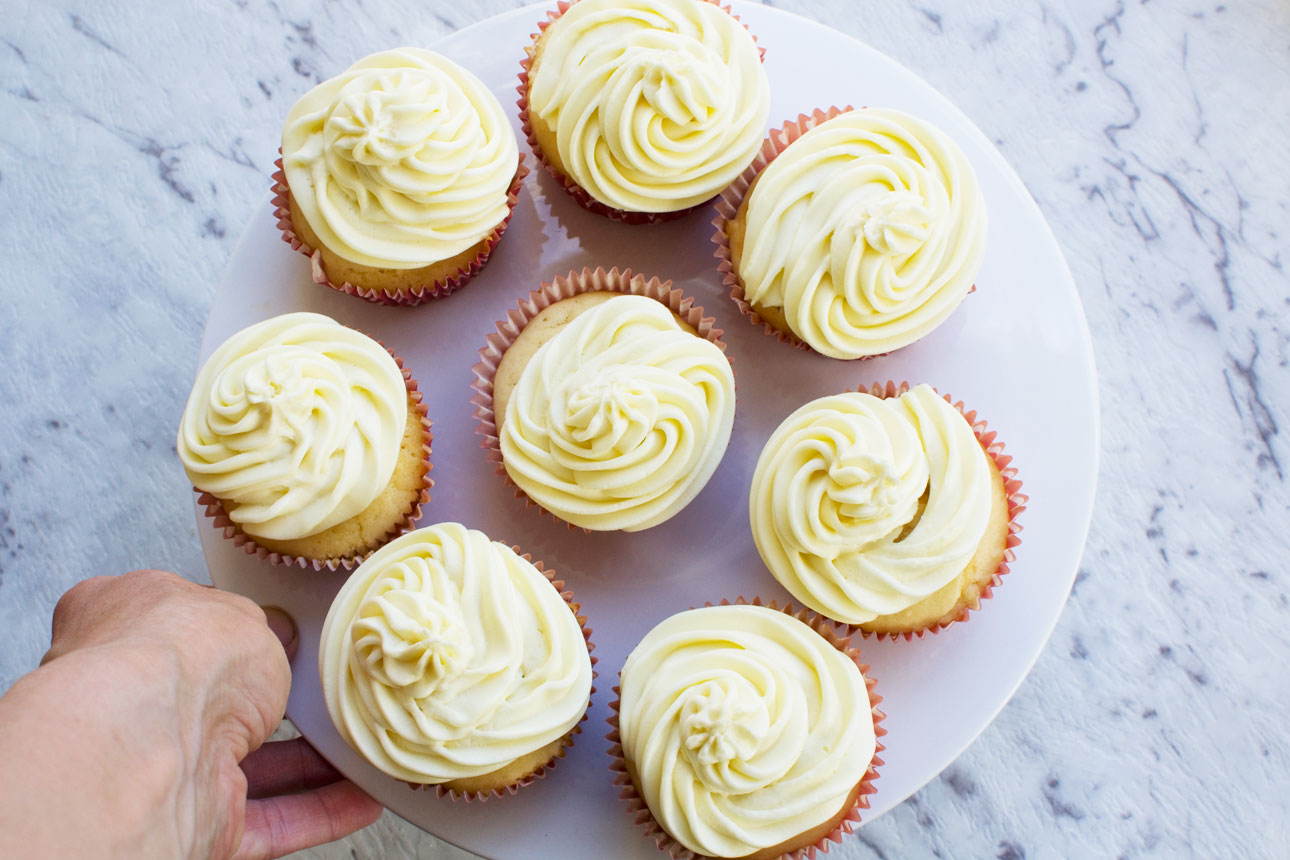 Someone holding a plate of healthier vanilla cupcakes with 2-ingredient frosting