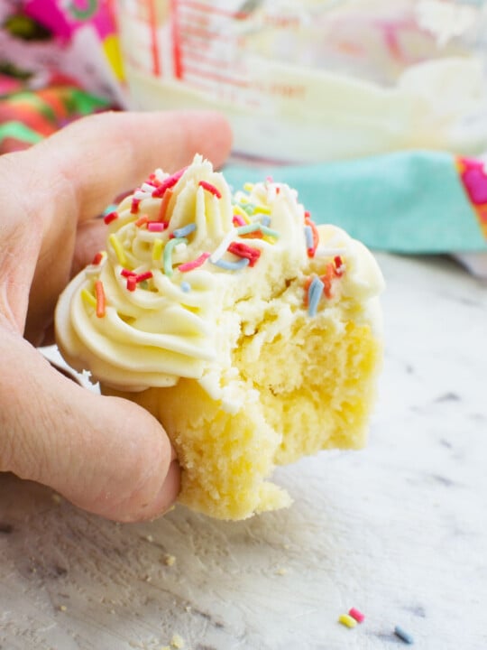 A close up of someone holding a vanilla cupcake with a bite out of it