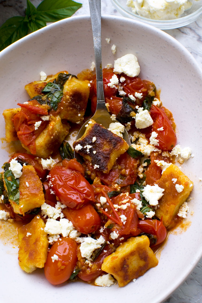 A close up of some crispy pan fried gnocchi in cherry tomato sauce in a white bowl with a spoon