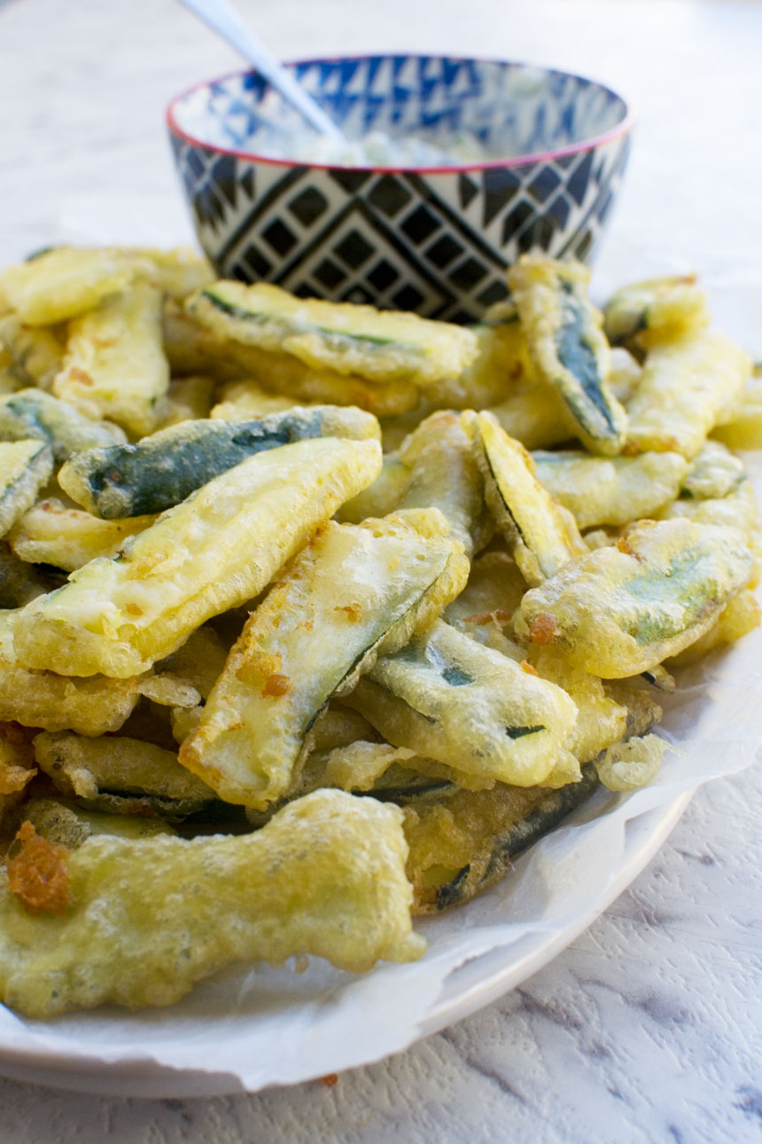 A big plate of zucchini fries with a bowl of tzatziki in the background