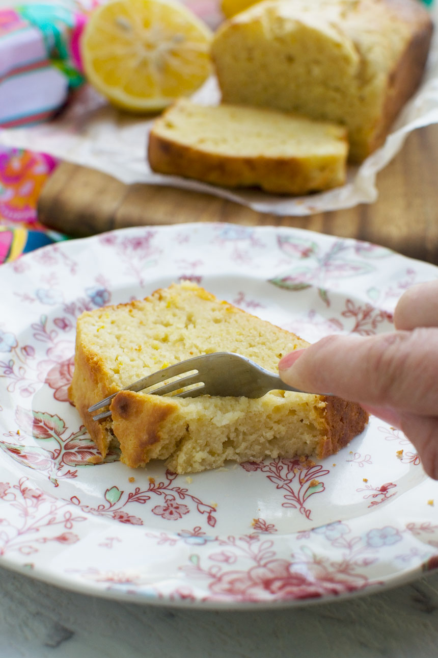 A slice of ricotta lemon loaf cake on a plate - someone eating it with a fork