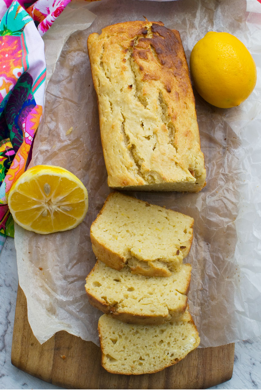 A ricotta lemon loaf cake sliced on a wooden cutting board - with some lemons