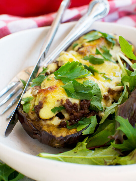 A close up of a white plate of Greek stuffed eggplant or papoutsakia served with a green salad