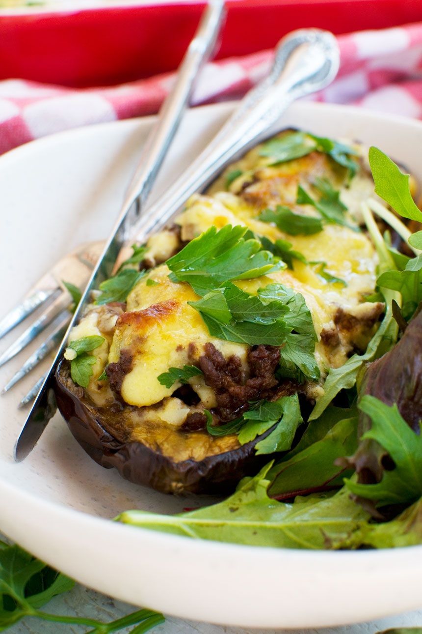 A close up of a white plate of Greek stuffed eggplant or papoutsakia served with a green salad