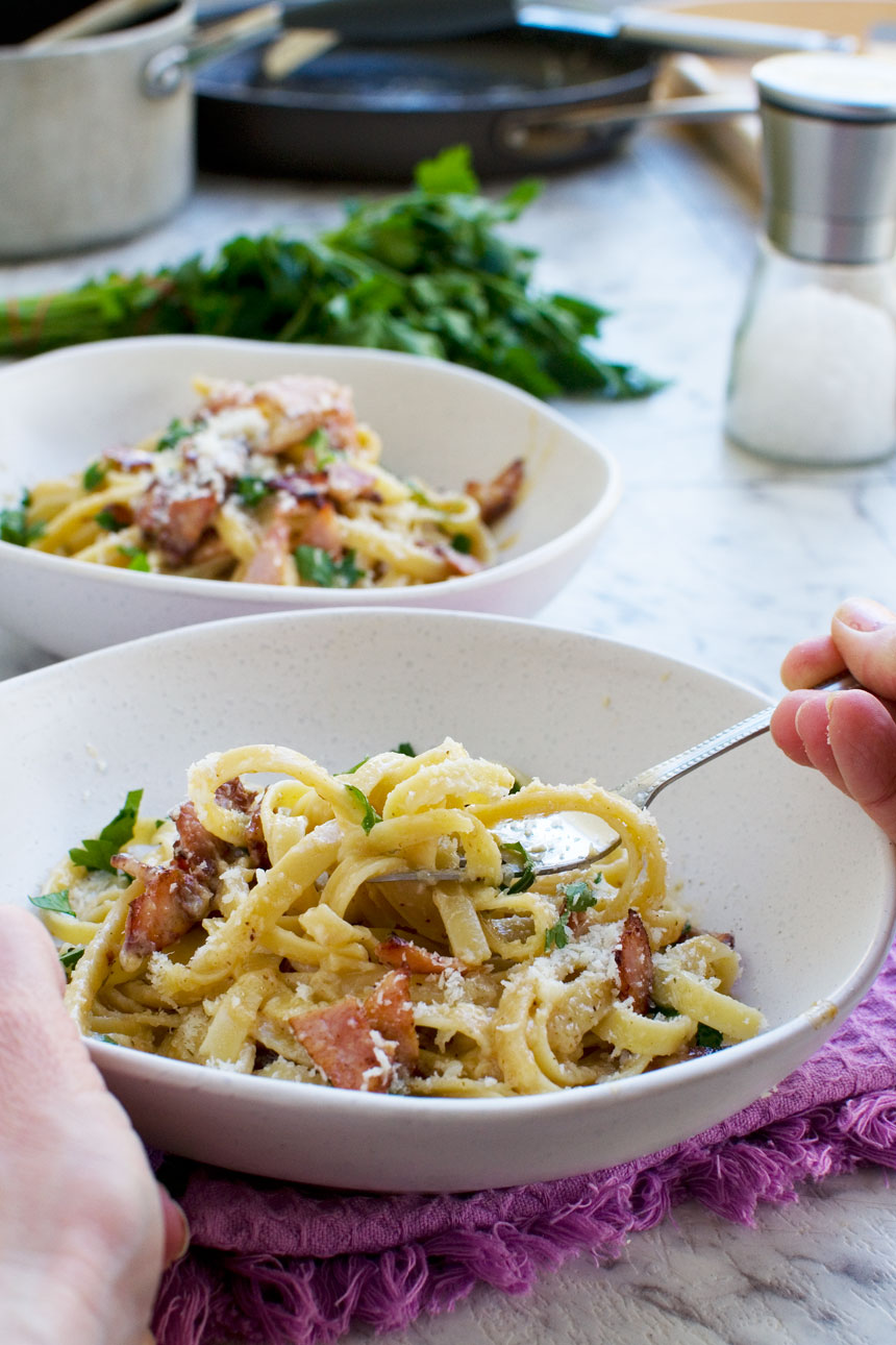 Someone eating a bowl of pasta carbonara without cream with another bowl in the background