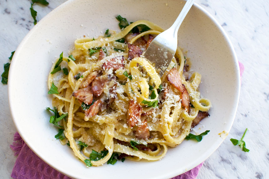 A closeup of a white bowl of pasta carbonara without cream from above