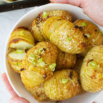 Someone holding out a bowl of mini hasselback potatoes with parmesan and garlic