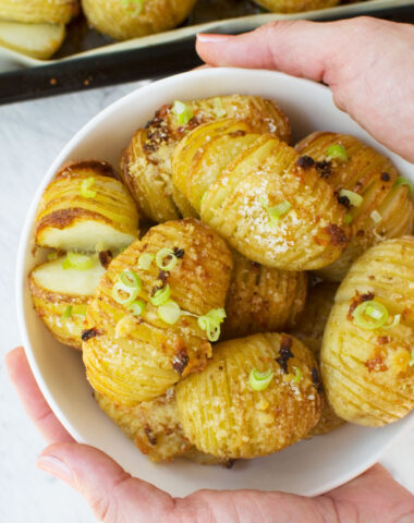Someone holding out a bowl of mini hasselback potatoes with parmesan and garlic