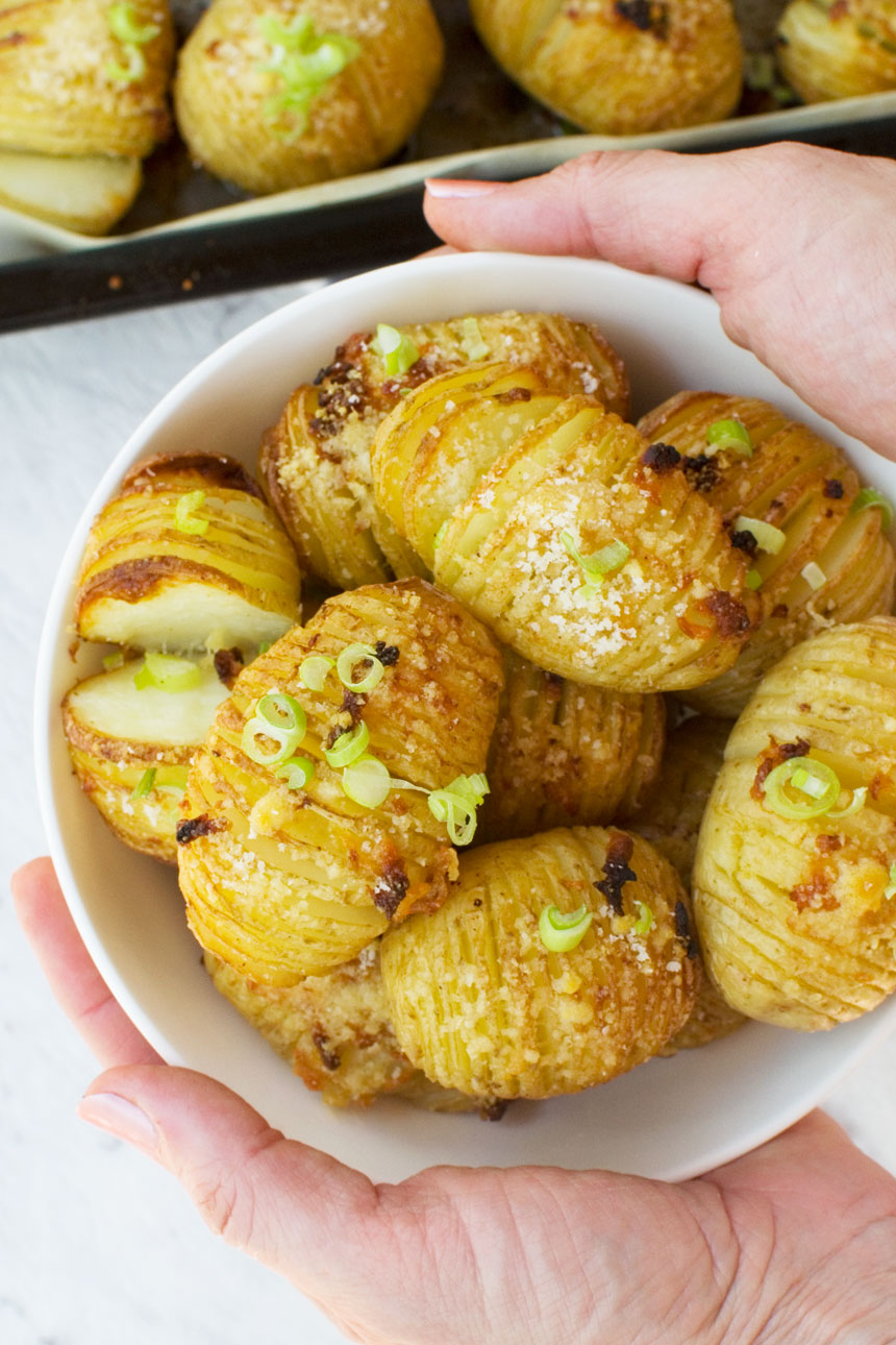 Someone holding out a bowl of mini hasselback potatoes with parmesan and garlic