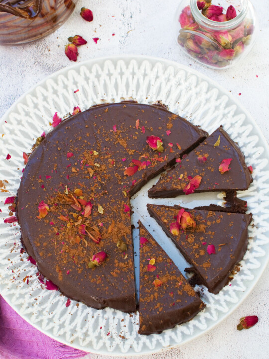 A no bake chocolate truffle cake on a grey patterned plate sliced and decorated with rose buds
