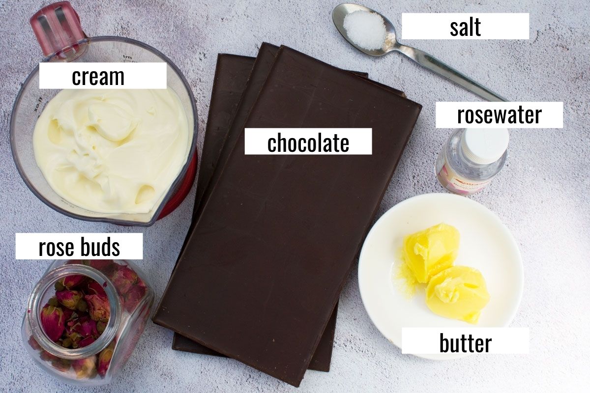 An image showing 6 ingredients for making a no bake chocolate truffle cake: cream, chocolate, butter, salt, rose buds, salt, rosewater