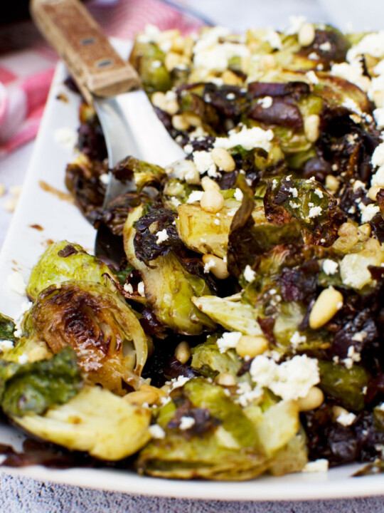 A plate of honey balsamic brussels sprouts with pine nuts and feta with a spoon in it