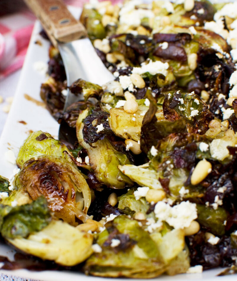 A plate of honey balsamic brussels sprouts with pine nuts and feta with a spoon in it