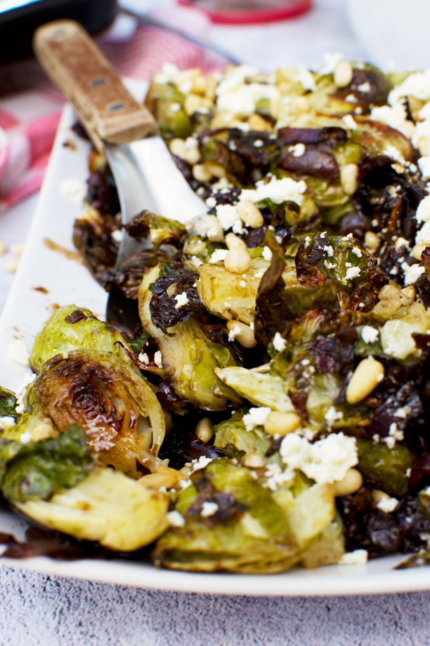 A plate of honey balsamic brussels sprouts with pine nuts and feta with a spoon in it
